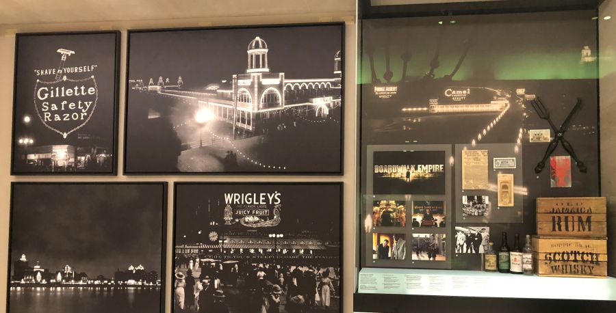 Photograph of Boardwalk Empire exhibit case with photographs and artifacts depicting the Boardwalk at night with lights, the HBO Boardwalk Empire television show and props from the show. .